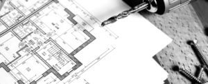 Blueprints on a table with screws and a power drill