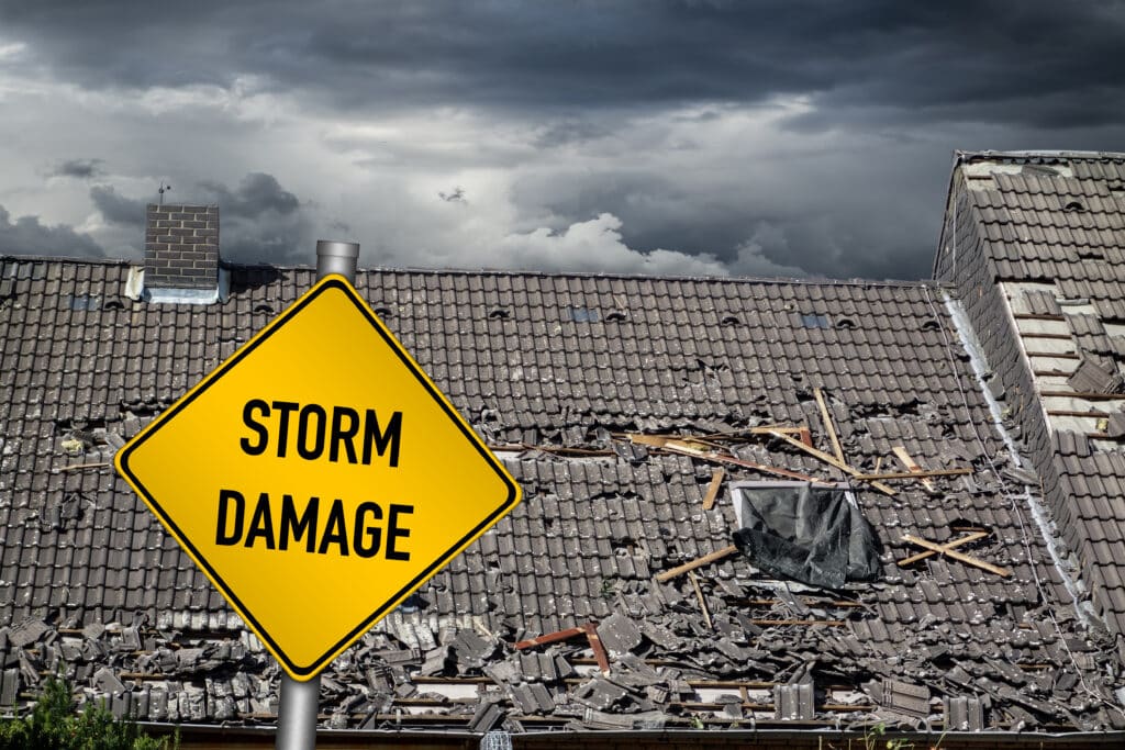 yellow damage warning sign in front of roof of house damaged by heavy hurricane tornado storm