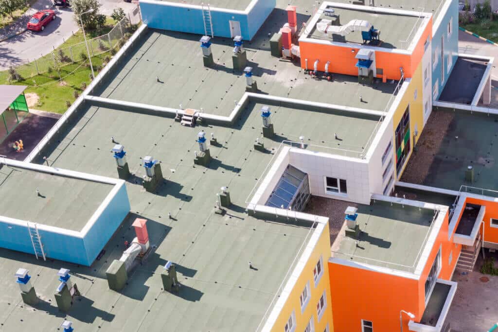 Top view flat roof with air conditioners and hydro insulation membranes on top of a modern blue and orange apartment building sunny summer day.